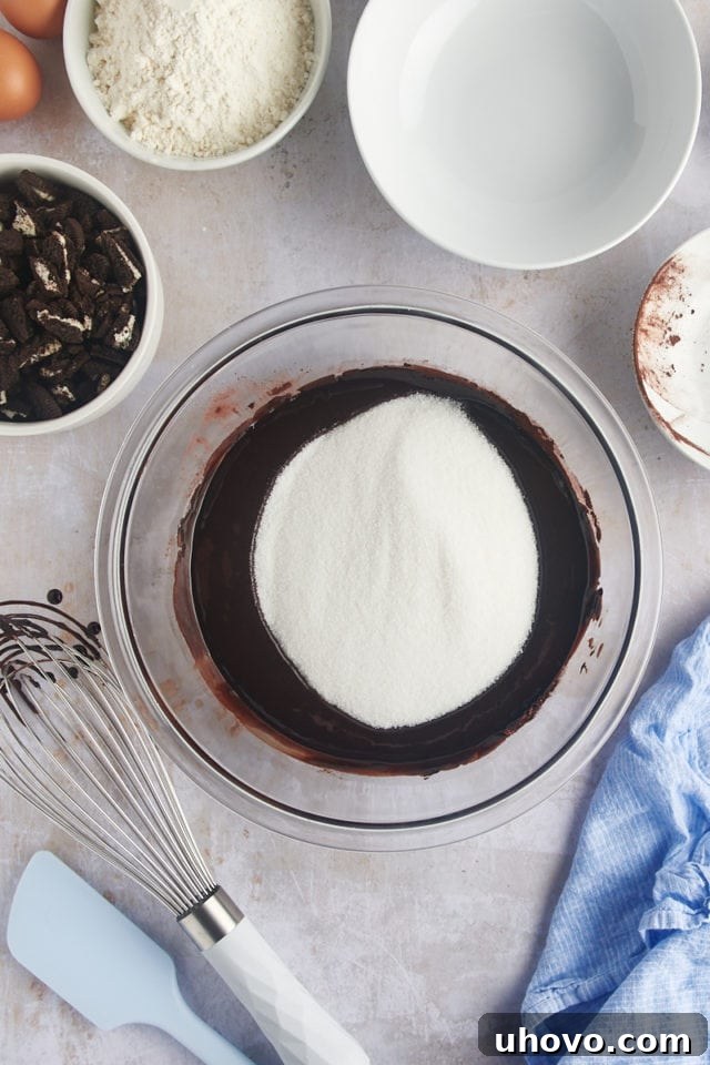 Overhead view of granulated sugar being added to the wet ingredients for the brownie batter.