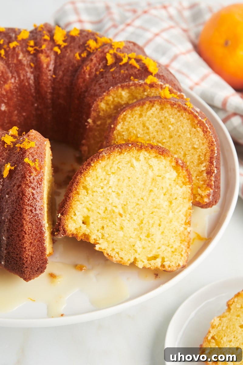 A beautifully sliced orange pound cake on a white cake plate, revealing its moist interior and golden crust.