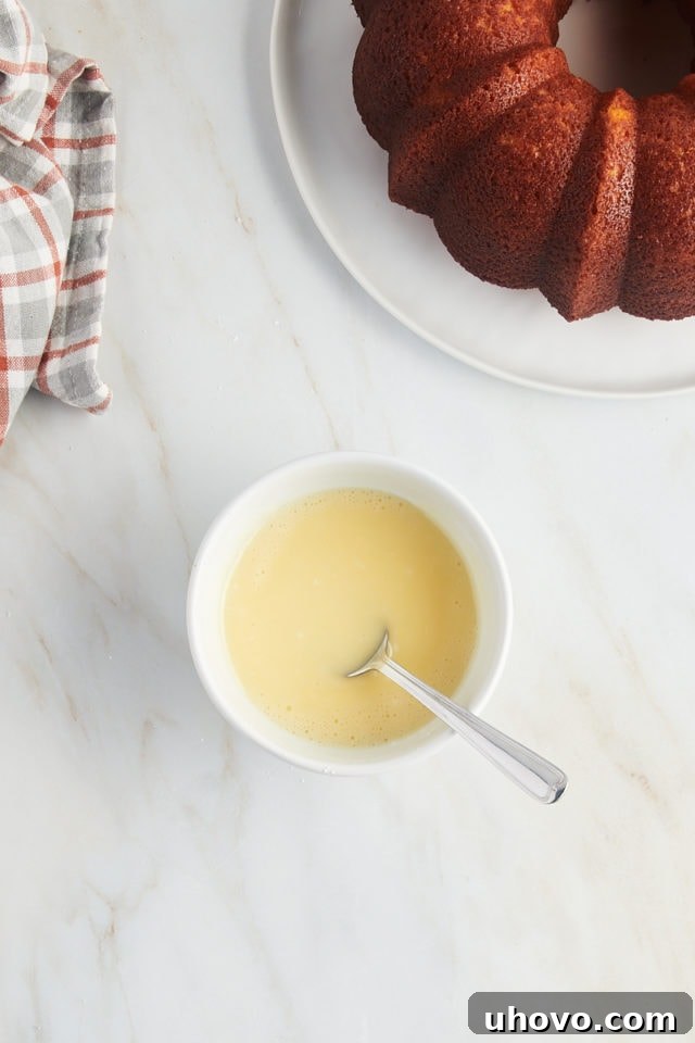 Overhead view of a perfectly mixed orange glaze in a white bowl, smooth and ready to be drizzled over the cake.