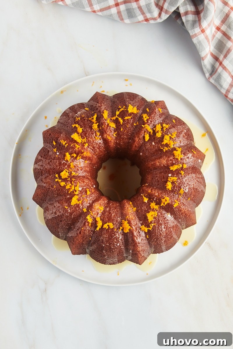 A gorgeously glazed orange pound cake, topped with fresh orange zest, presented on a pristine white cake plate.