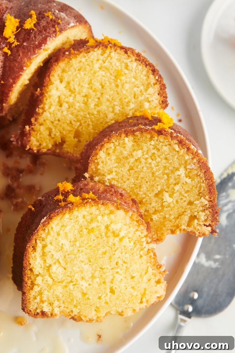 Three perfectly cut slices of orange pound cake, artfully overlapping on a white cake plate, highlighting their moist texture.