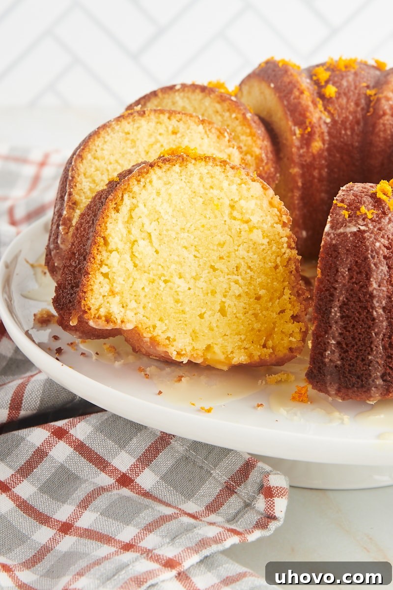 A partially sliced orange pound cake, gracefully positioned on a white cake stand, showcasing its inviting texture.