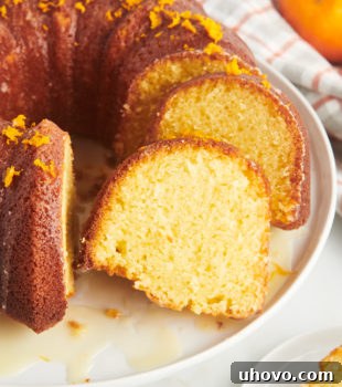 A partially sliced orange pound cake on a white cake plate