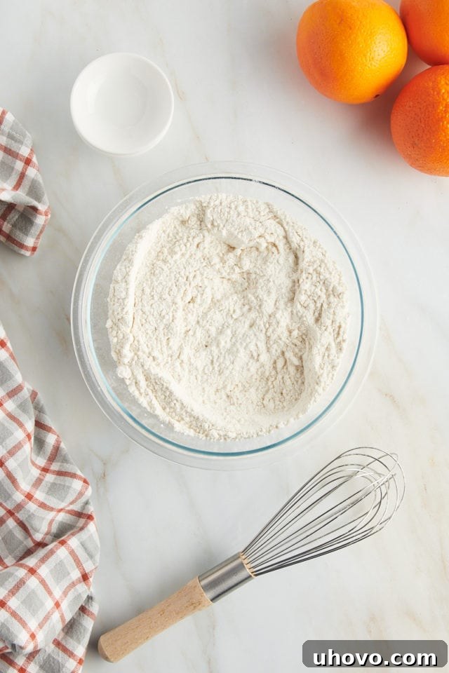 Overhead view of a glass mixing bowl containing flour, baking powder, baking soda, and salt, perfectly combined.