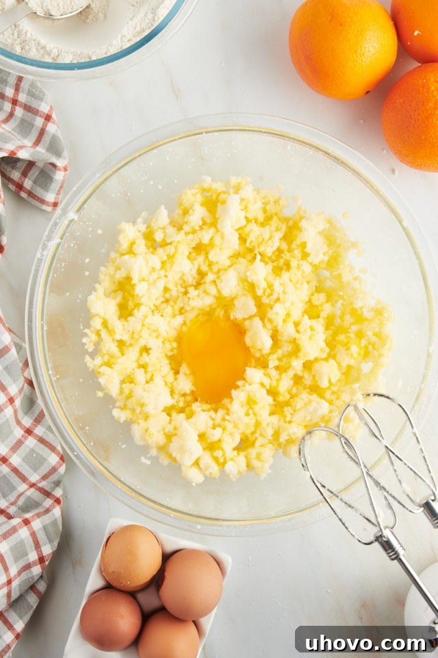 Overhead view of an egg freshly added to the creamed butter and sugar mixture in a glass mixing bowl, ready to be incorporated.