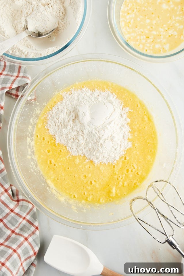 Overhead view of the dry ingredients being carefully added to the wet ingredients in a large mixing bowl, alternating for proper incorporation.