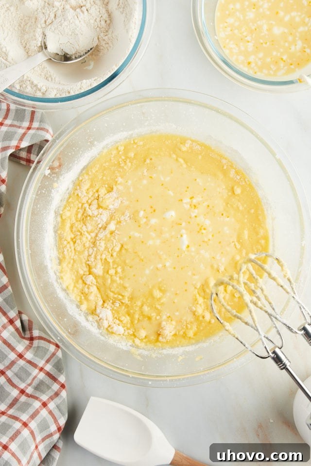 Overhead view of the orange juice mixture being poured into the pound cake batter, carefully incorporating the citrus liquids.