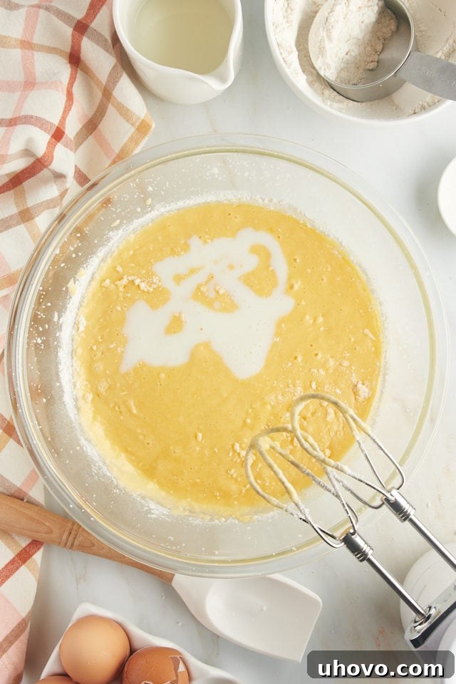 Buttermilk being poured into the cake batter, ensuring a moist and tender texture through its reaction with the leavening agents.