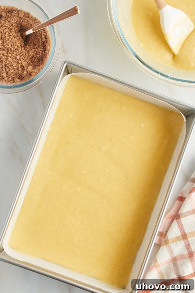 Half of the luscious yellow cake batter is evenly spread in the prepared baking pan, forming the base layer for the honey bun cake.