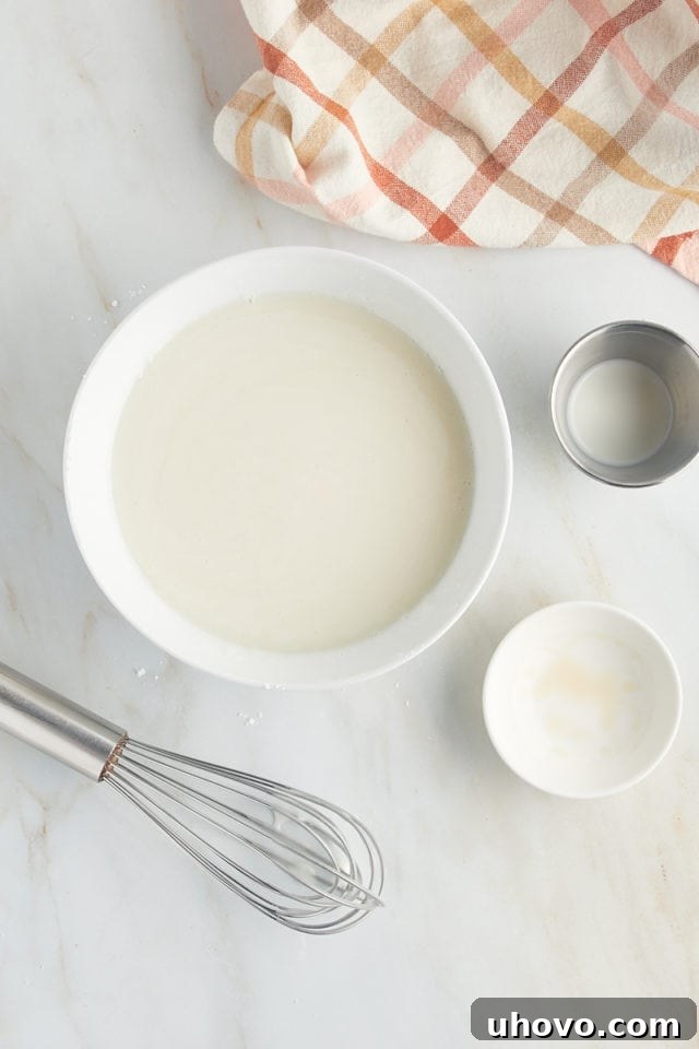 A smooth, white vanilla glaze in a mixing bowl, perfectly prepared to top the warm honey bun cake, adding a final touch of sweetness.