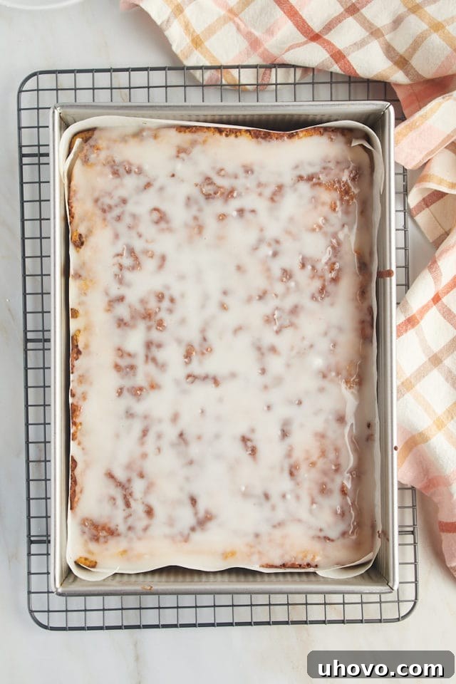 The finished honey bun cake in its pan, beautifully coated with a smooth vanilla glaze, cooling on a wire rack and ready to be served.