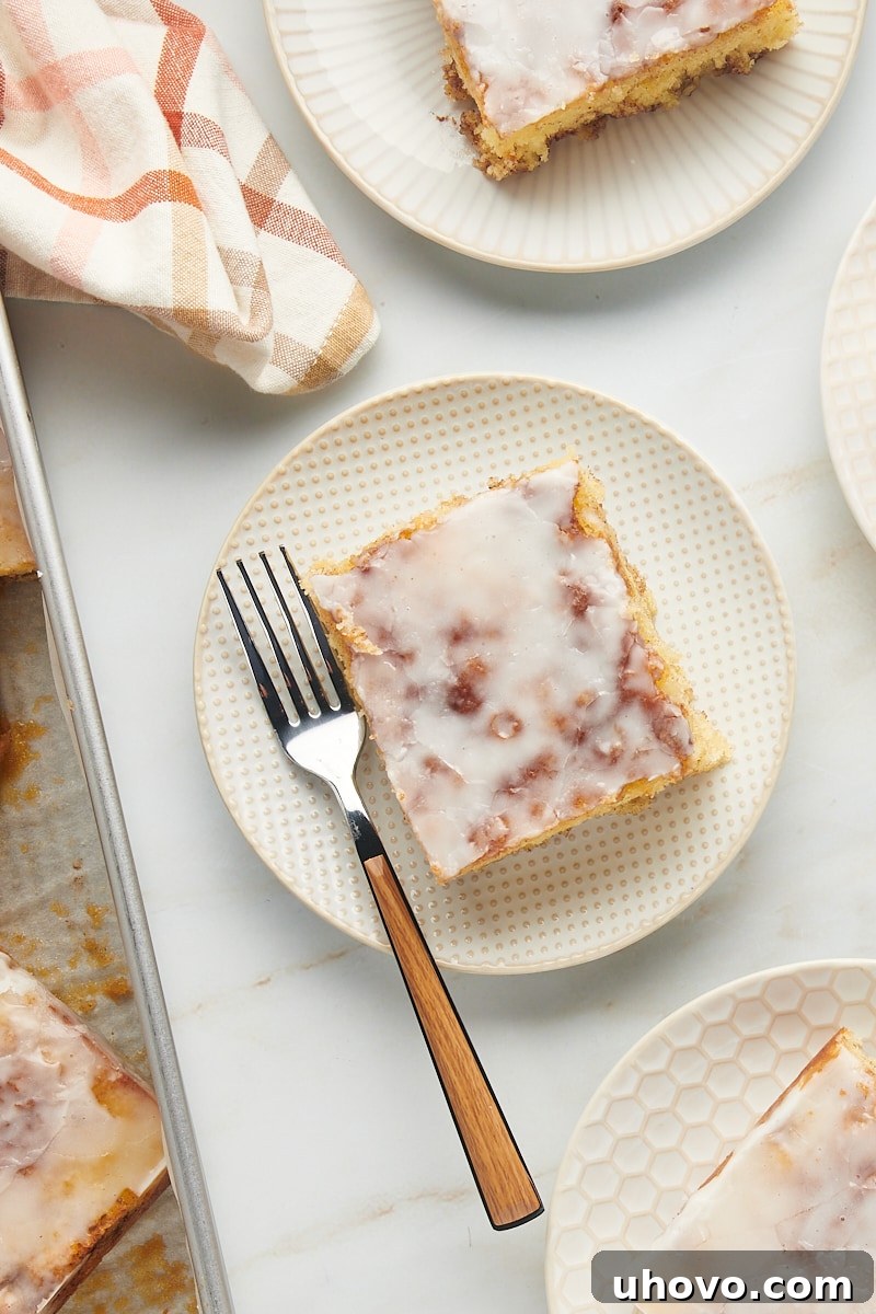 Two plates each holding a generous slice of honey bun cake, perfectly showing the cinnamon swirl and vanilla glaze, inviting you to take a bite.