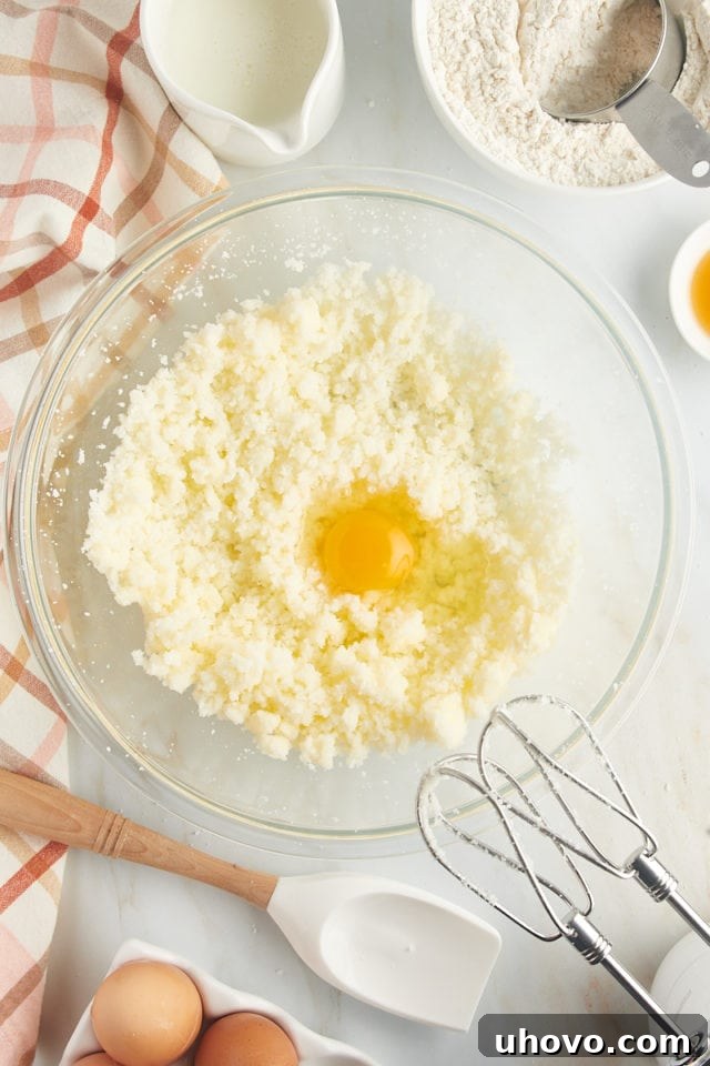 A close-up of an egg being gently cracked and added to the creamy mixture of butter and sugar, ensuring proper incorporation into the cake batter.