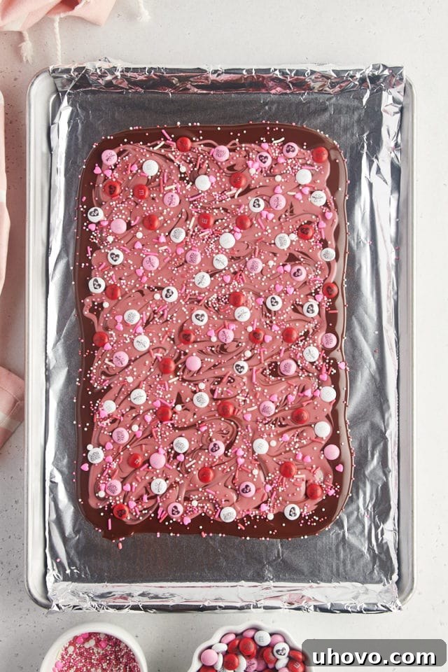 Overhead view of sprinkles being added to the dark and ruby chocolate marbled bark, completing the festive look.