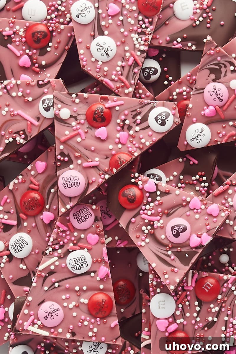 Overhead close-up view of irregularly shaped pieces of marbled Valentine's bark, showing the intricate chocolate swirls and colorful toppings.