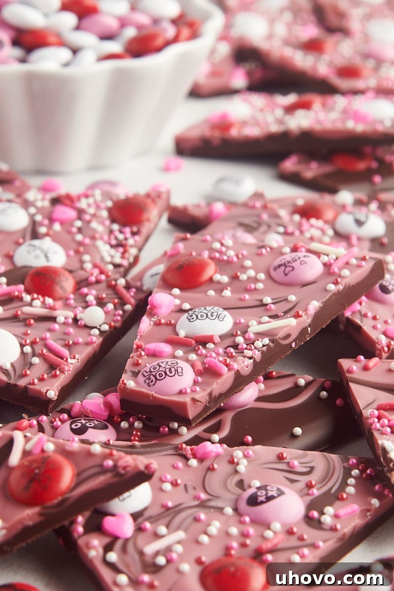 Marbled Valentine's bark piled on a plate with a bowl of M&M candies in the background, ready to be enjoyed.