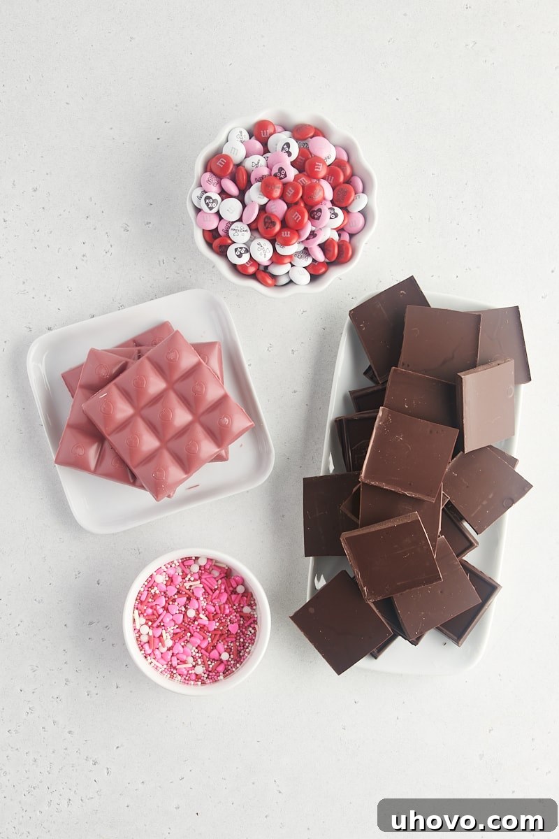 Overhead view of ingredients for marbled Valentine's bark, including dark chocolate, ruby chocolate, M&Ms, and sprinkles.