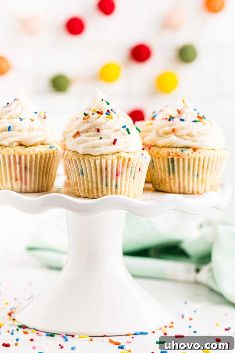 A festive arrangement of confetti cupcakes on a white cake stand, with colorful garland draped charmingly in the background, signaling a celebration.