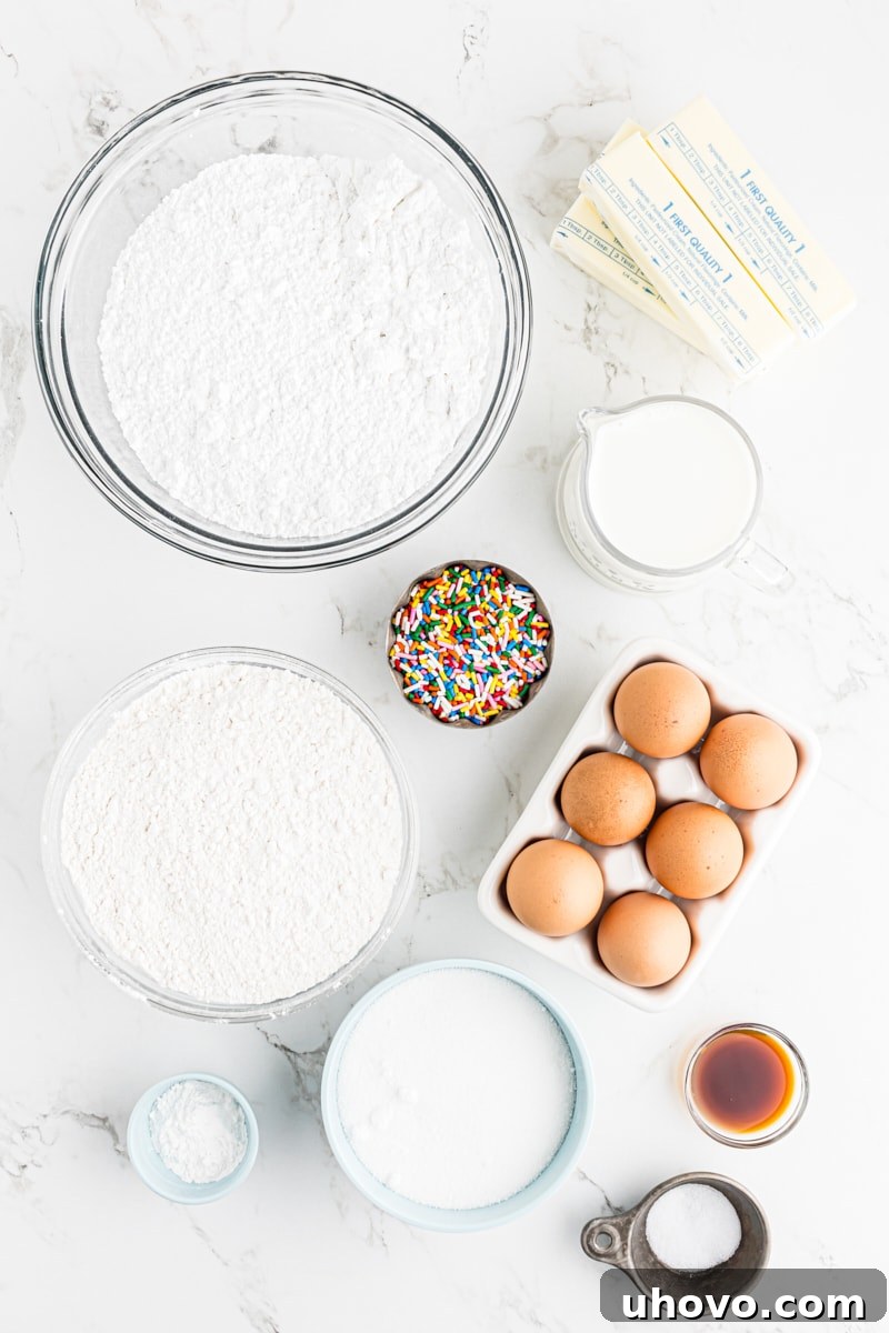 An overhead view showcasing all the essential ingredients neatly arranged on a white surface, ready for making confetti cupcakes.