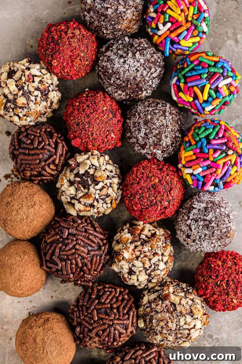 An overhead view of an assortment of homemade chocolate truffles, some coated in cocoa powder, some in sprinkles, and others in chopped nuts, arranged on a baking sheet, ready for serving or gifting.