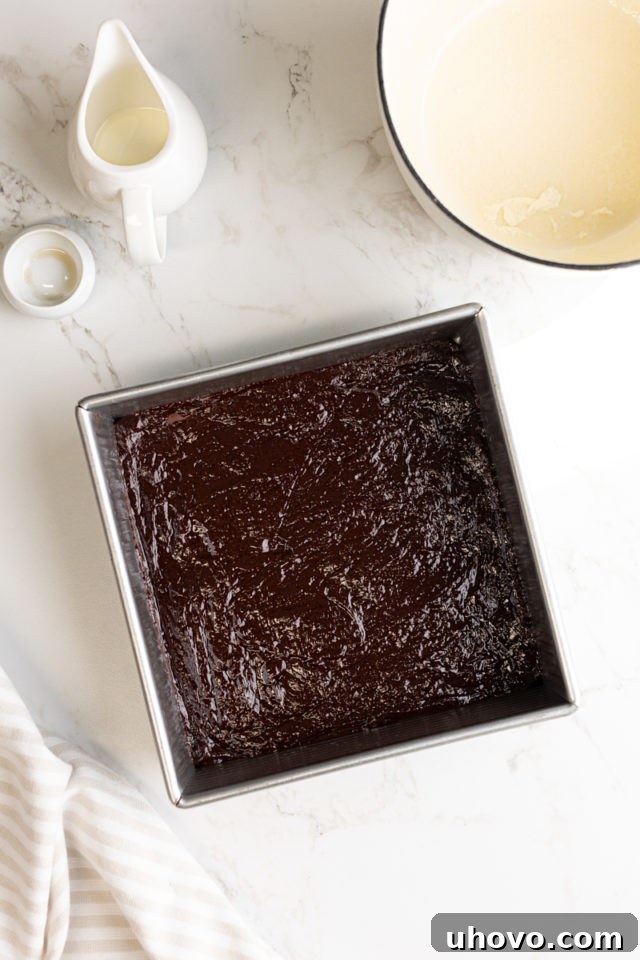The smooth chocolate truffle mixture (ganache) spread evenly in a square baking pan, preparing it for chilling and setting.