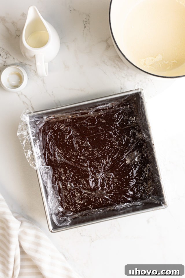 The square pan containing the chocolate truffle mixture, now covered tightly with plastic wrap directly on its surface, ready to be refrigerated.
