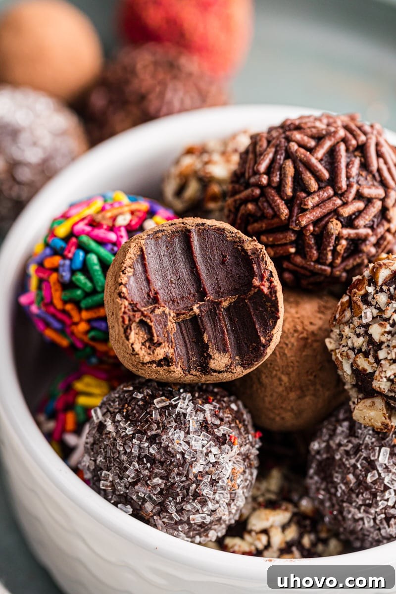 A delectable homemade chocolate truffle with a bite taken out, revealing its rich ganache interior, resting atop a pile of other truffles in a white bowl, tempting to eat.