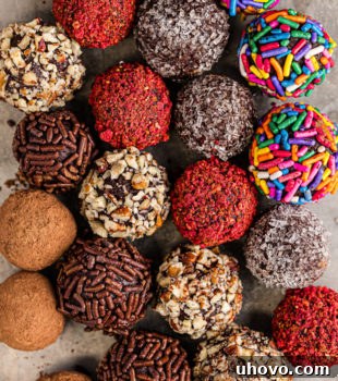 An overhead view of an assortment of homemade chocolate truffles, some coated in cocoa powder, some in sprinkles, and others in chopped nuts, arranged on a baking sheet, ready for serving or gifting.