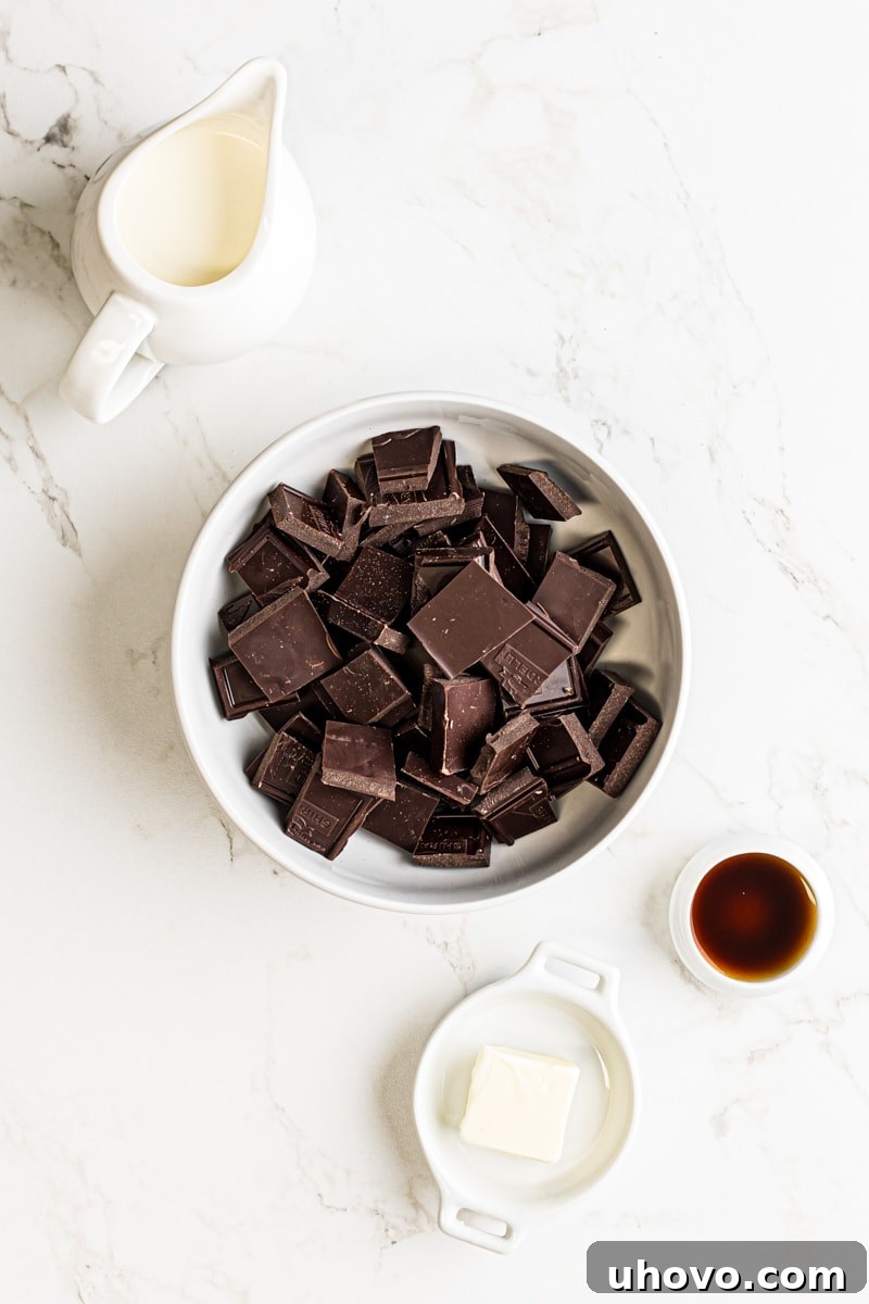 An overhead view of the simple ingredients needed for making homemade chocolate truffles: chopped dark chocolate, softened butter, heavy cream, and a bottle of vanilla extract.