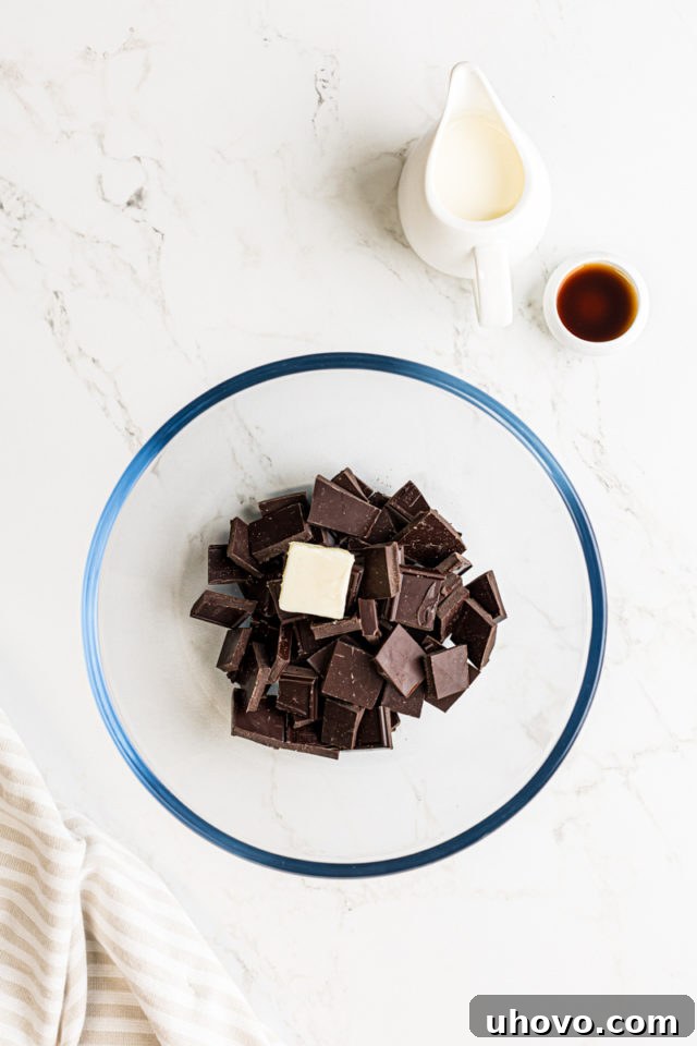 An overhead view of finely chopped dark chocolate and softened unsalted butter placed together in a clear glass mixing bowl, ready for the ganache making process.