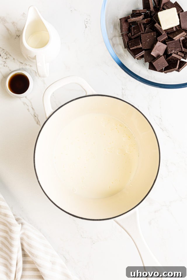 An overhead shot showing heavy cream gently simmering in a small saucepan on a stovetop, indicating it's heating up for the ganache.