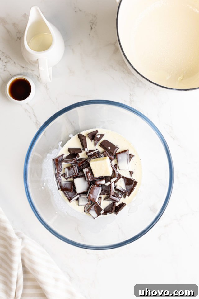 Hot heavy cream being carefully poured over the chopped chocolate and butter in a glass bowl, initiating the melting process for the ganache.