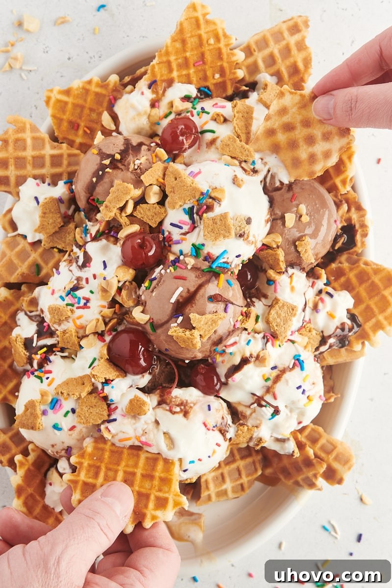 A large white plate of ice cream nachos with two hands reaching in, each holding a spoon, ready to enjoy the communal dessert experience.
