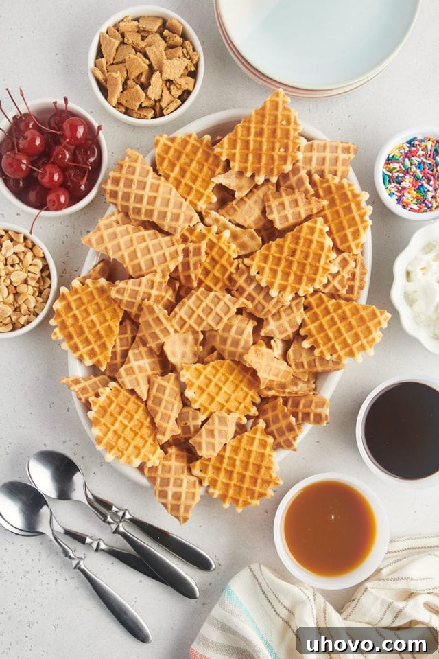 Overhead view of several waffle cones expertly broken into irregular, chip-like pieces, layered on a pristine white oval serving platter, ready for the next step of nacho assembly.