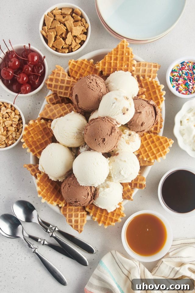 A close-up, overhead view of multiple scoops of vanilla, chocolate, and cookie dough ice cream carefully placed atop the broken waffle cone chips on a white platter, forming the second layer of the nachos.