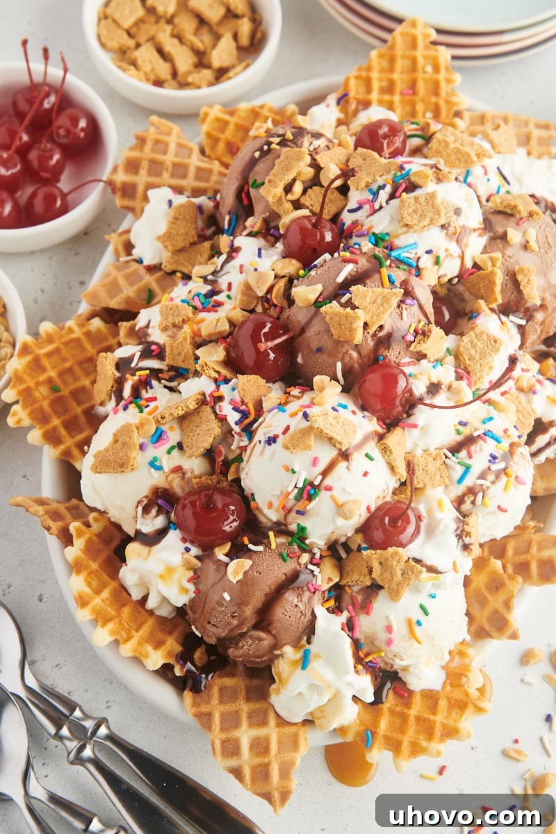 A wide shot of a large white serving platter filled with an abundant amount of ice cream nachos, surrounded by small, colorful bowls brimming with various toppings.