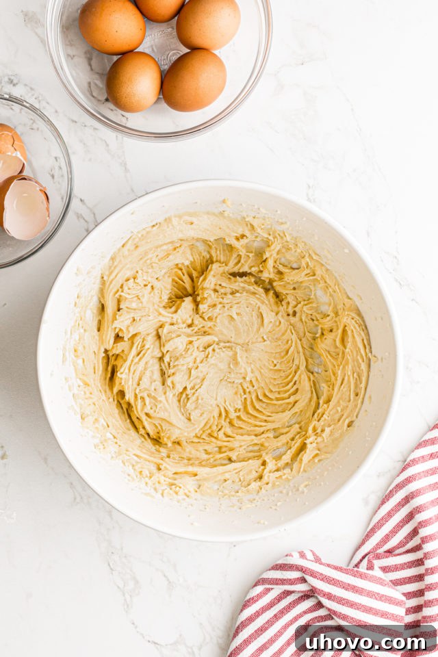 Smooth and glossy pâte à choux dough after all eggs have been mixed in, resting in a white mixing bowl, indicating ideal consistency for piping.