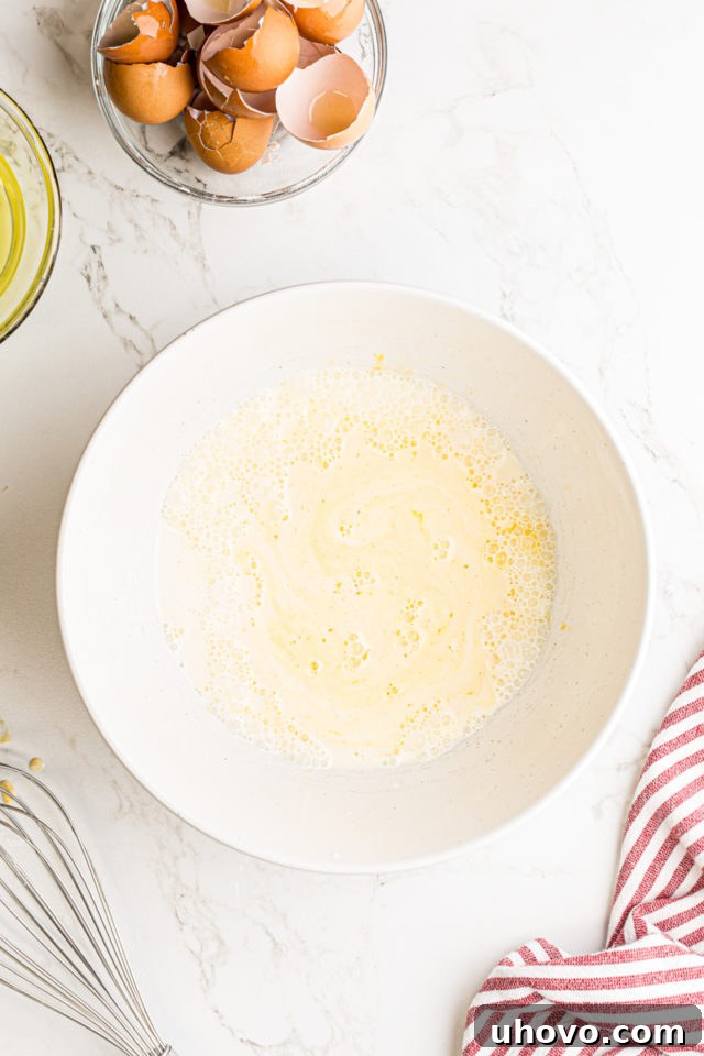 Overhead view of milk, heavy cream, and five egg yolks whisked together in a white mixing bowl, forming the base for the pastry cream.