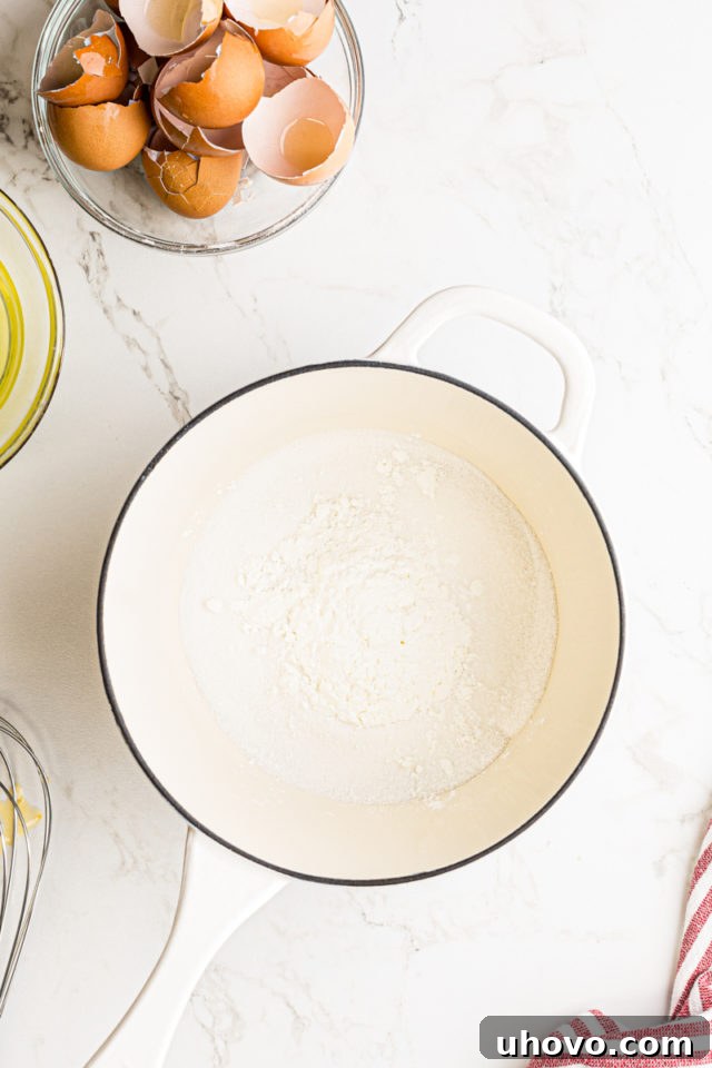 Overhead view of granulated sugar, salt, and cornstarch dry-mixed in a saucepan before the liquid ingredients are added for the pastry cream.