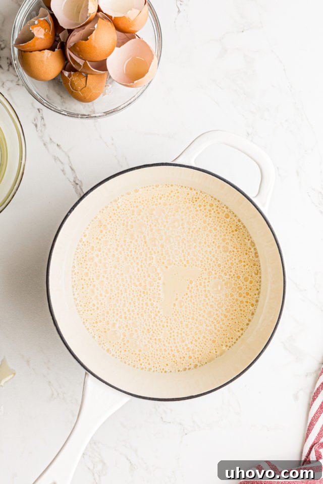 All combined ingredients for the pastry cream, including milk, cream, egg yolks, sugar, salt, and cornstarch, thoroughly whisked in a saucepan before heating.