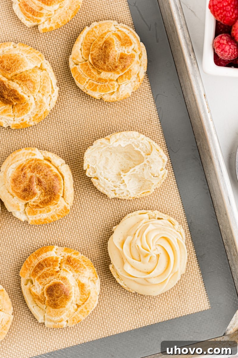 Close-up overhead view of a freshly baked cream puff being filled with luxurious pastry cream using a piping bag with a star tip.