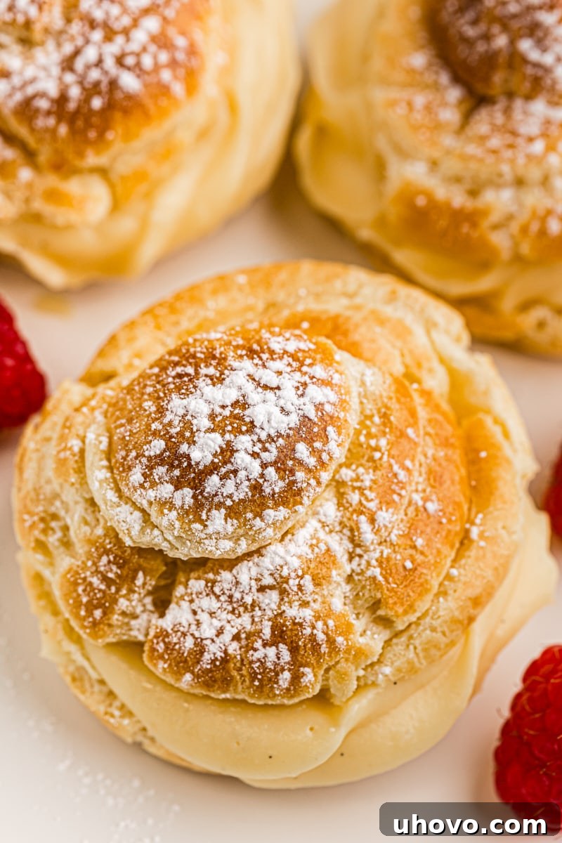 A close-up view of a single, perfectly golden cream puff, showing its delicate texture and the creamy filling peeking out, on a white plate.