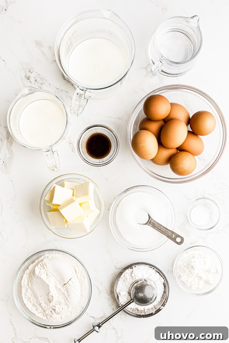 Overhead view of various ingredients for making cream puffs laid out on a clean surface, including butter, eggs, milk, flour, and sugar.