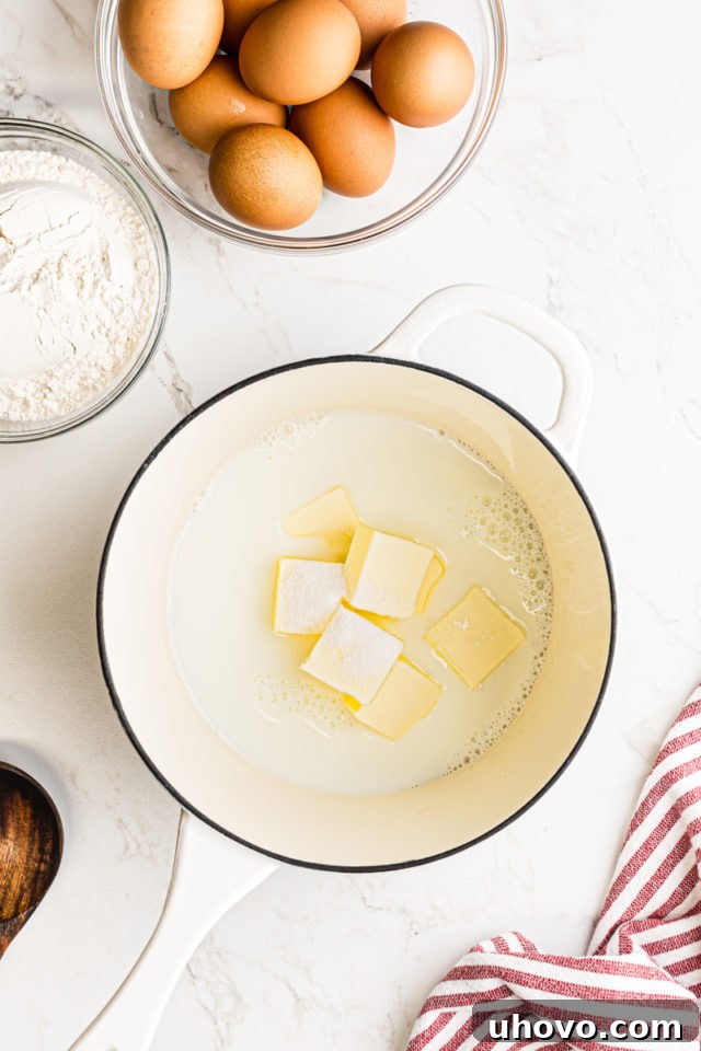 Overhead view of milk, water, granulated sugar, cubed butter, and a pinch of salt simmering in a saucepan.