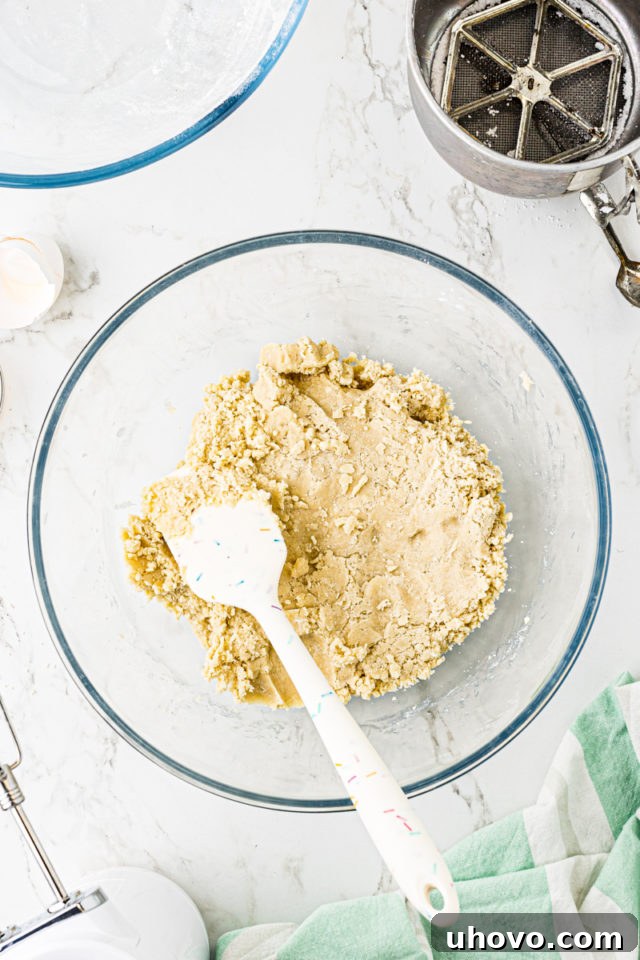 Overhead view of fully mixed Lofthouse cookie dough in a glass mixing bowl, being given a final stir with a spatula.