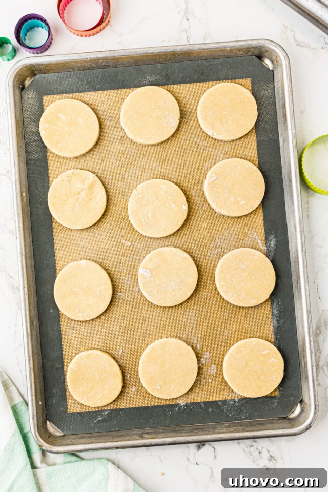 Overhead view of several perfectly cut-out Lofthouse cookie dough rounds neatly arranged on a baking sheet lined with a silicone mat.