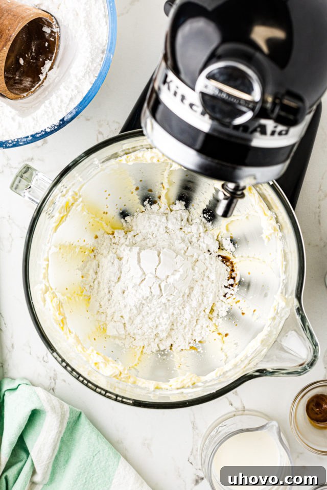 Overhead view of confectioners' sugar being gradually added to the frosting mixture in a stand mixer.