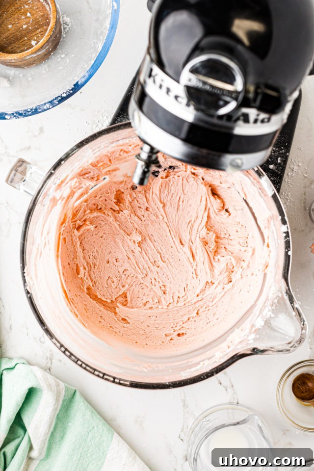 Overhead view of vibrant pink frosting in the bowl of a stand mixer, smooth and ready.