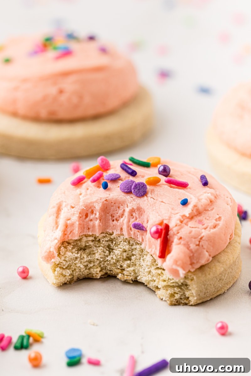 A frosted Lofthouse cookie with a bite taken out, showing its soft interior, with more cookies visible in the blurred background.