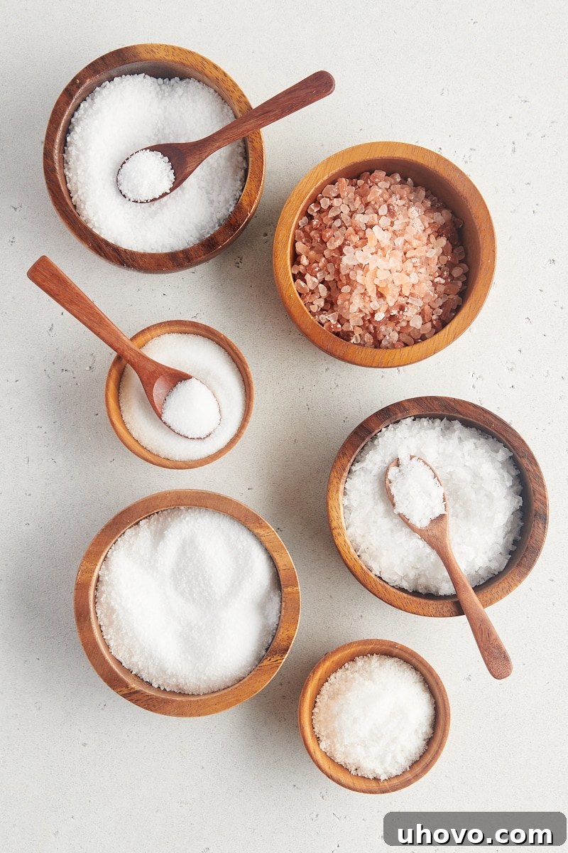overhead view of table salt, kosher salt, sea salt, and Himalayan pink salt in small wooden bowls